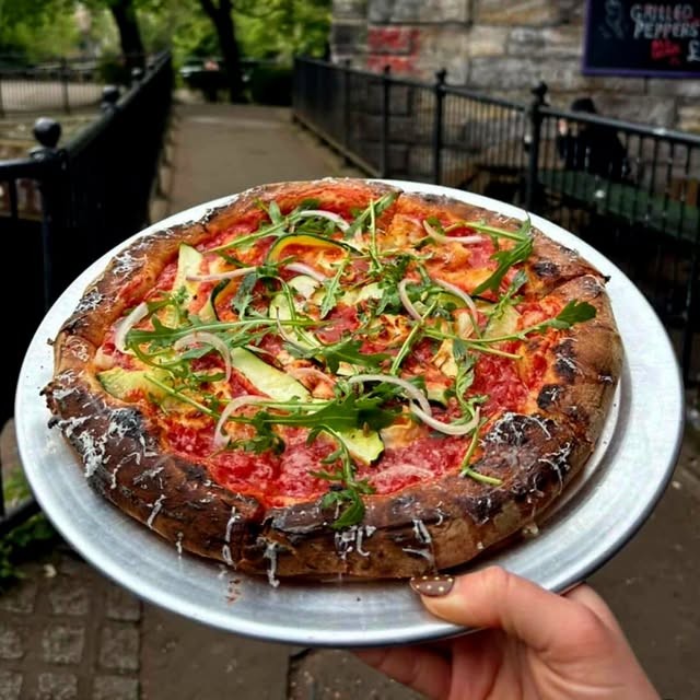 Pizza with rocket held up outside by the River Kelvin